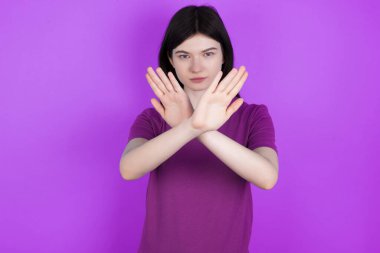 Genç esmer kadının reddedilme ifadesi var. Kollarını kavuşturuyor ve avuç içleri negatif işaretler veriyor. Öfkeli yüz ifadesi..