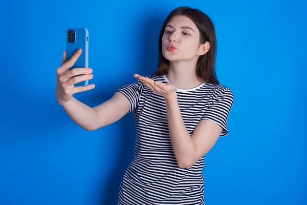 若い女性がスマートフォンのカメラでエアキスを吹いて自撮りしオンライン通話でMwahを送る — ストック写真
