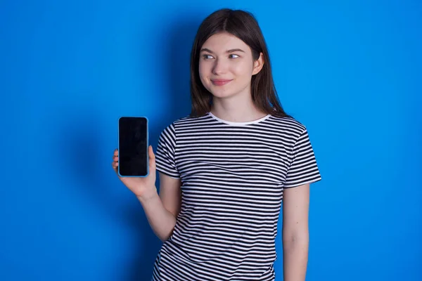 young woman holds new mobile phone and looks mysterious aside shows blank display of modern cellular