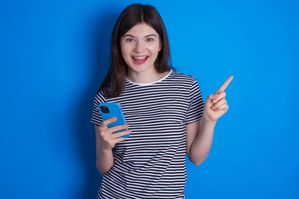 Mujer Joven Asombrada Sosteniendo Teléfono Señalando Con Dedo Lado Espacio —  Fotos de Stock