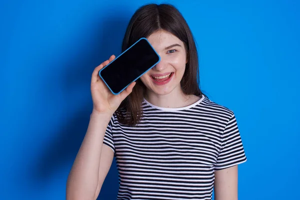 Mujer Joven Sosteniendo Teléfono Inteligente Moderno Cubriendo Ojo Mientras Sonríe — Foto de Stock