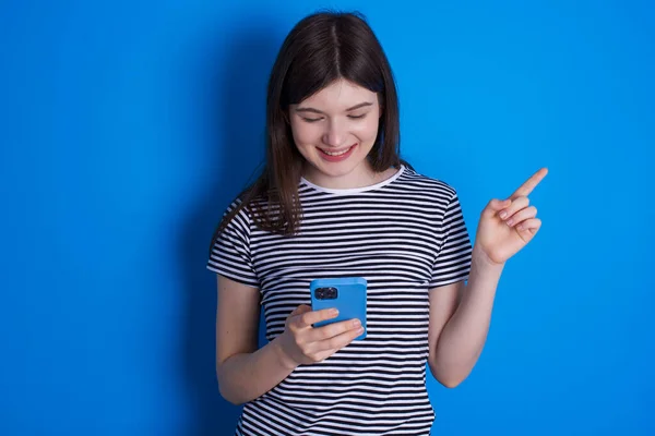 Sorrindo Jovem Apontando Com Dedo Para Espaço Branco Segurando Telefone — Fotografia de Stock