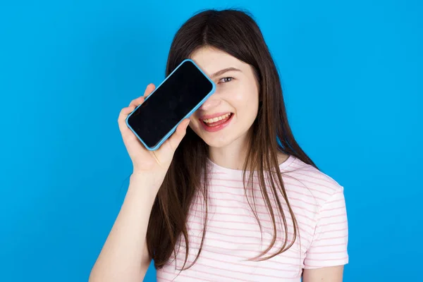 Young Brunette Woman Holding Modern Smartphone Covering One Eye While — Fotografia de Stock