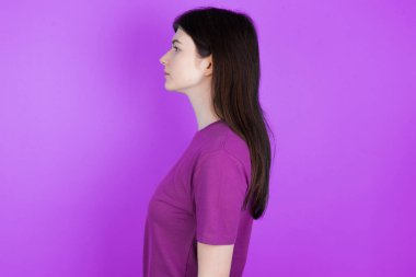 Genç esmer kadın yan tarafa bakıyor, rahat profil pozu veriyor kendine güvenen bir gülümsemeyle doğal bir yüz ifadesi var..