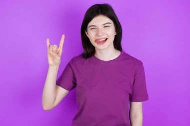 Genç esmer kadın kaya hareketi yapıyor ve kameraya gülümsüyor. En sevdiği konsere gitmeye hazır..