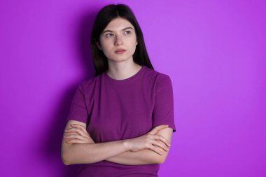 Charming thoughtful young brunette woman stands with arms folded concentrated somewhere with pensive expression thinks what to do