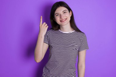 young brunette woman smiling and looking friendly, showing number one or first with hand forward, counting down