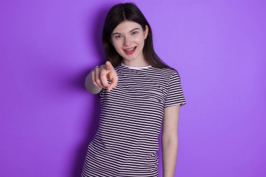 Excited positive young brunette woman points index finger directly at you, sees something very funny. Wow, amazing