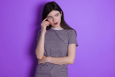 Astonished young brunette woman looks aside surprisingly with opened mouth.