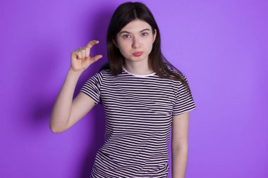 young brunette woman purses lip and gestures with hand, shows something very little.