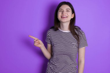 young brunette woman laughs happily points away on blank space demonstrates shopping discount offer, excited by good news or unexpected sale.