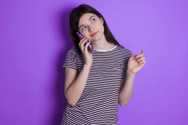 young brunette woman speaks on mobile phone spends free time indoors calls to friend.