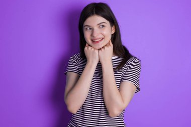 young brunette woman holds hands under chin, glad to hear heartwarming words from stranger