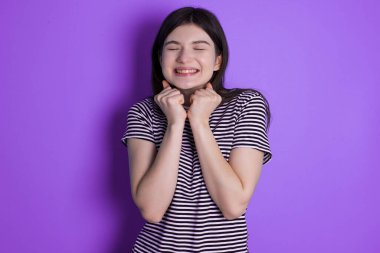 young brunette woman grins joyfully, imagines something pleasant, copy space. Pleasant emotions concept.