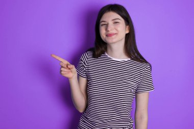 young brunette woman points to side on blank space demonstrates advertisement. People and promotion concept
