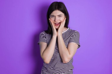 Upset young brunette woman touching face with two hands