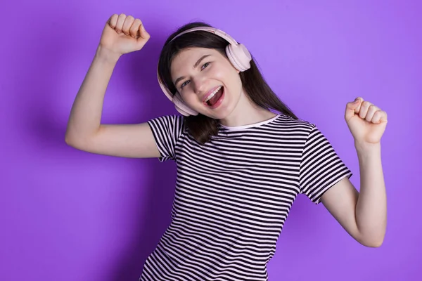 Carefree young brunette woman thick beard and toothy smile raises arms dances carefree moves with rhythm of music listens music from playlist via headphones