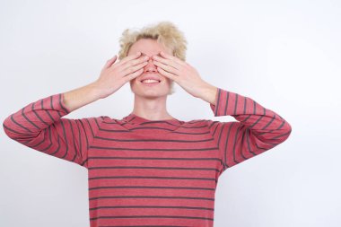 Genç sarışın adam elleri ile gözlerini kapatıyor neşeli ve komik gülümsüyor. Kör kavram.