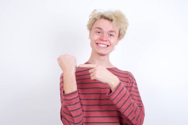 Sarışın genç adam kol saatini işaret ediyor, sabırsız, rahat bir ifadeyle kameraya bakıyor.