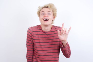 Genç sarışın adam kaya hareketi yapıyor ve kameraya gülümsüyor. En sevdiği konsere gitmeye hazır..