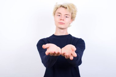 Sarışın genç adam avuç içi açık bir şey tutuyor ve kameraya sunuyor..