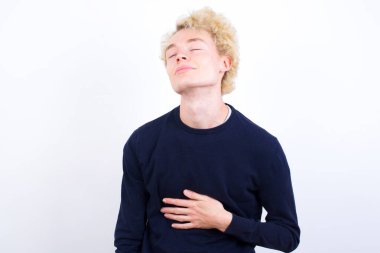 Genç sarışın adam karnına dokunuyor, nazikçe gülümsüyor, yemek yiyor ve tatmin oluyor..