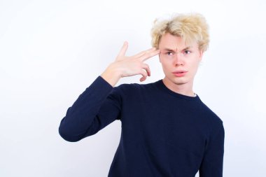 Mutsuz genç sarışın adam intihar jesti yapıyor ve tabancayı eliyle taklit ediyor, dudaklarını kıvırıyor, iki parmağını şakakta tutuyor.