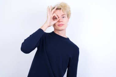 Genç beyaz adam el hareketleriyle gülümsüyor, gözleriyle mutlu yüzüyle parmaklarının arasından bakıyor..