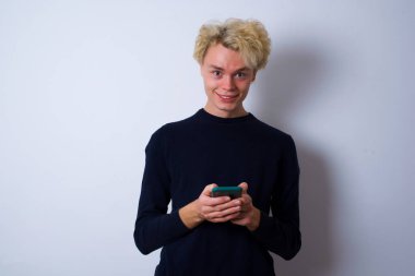 Genç beyaz adam uzak iletişimden hoşlanıyor, cep telefonu kullanıyor, hızlı ve sınırsız internet sörfü yapıyor, hoş bir gülümsemesi var, online alışveriş yapıyor.,