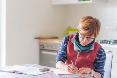 Evde çalışan, el yazısı ve kitap okuyan bir kadın.