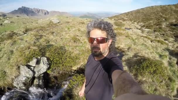 Homem adulto caucasiano caminhante com barba e óculos de sol tomando selfie no cume da montanha . — Vídeo de Stock