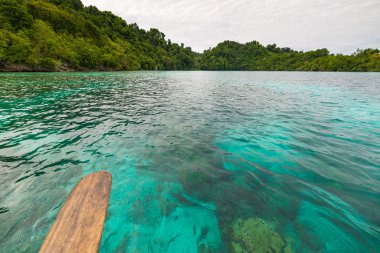 Şeffaf deniz, dramatik gökyüzü, uzak Malenge Plajı'nda geleneksel kültür ve yeşil orman, Togean Adaları, Sulawesi, Endonezya.
