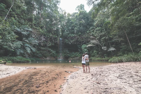 Couple of tourists looking at a stunning multicolored natural pool and waterfall in the rainforest of Lambir Hills National Park, Borneo, Malaysia. — Stock Photo, Image