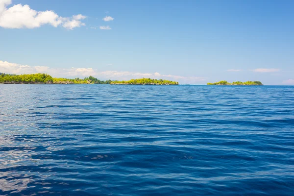 Felsige Küste der Insel, die von Inselchen getupft und von dichtem, sattgrünem Dschungel bedeckt ist, im farbenfrohen Meer der abgelegenen Togean Islands (oder togischen Inseln), Zentralsulawesi, Indonesien. — Stockfoto