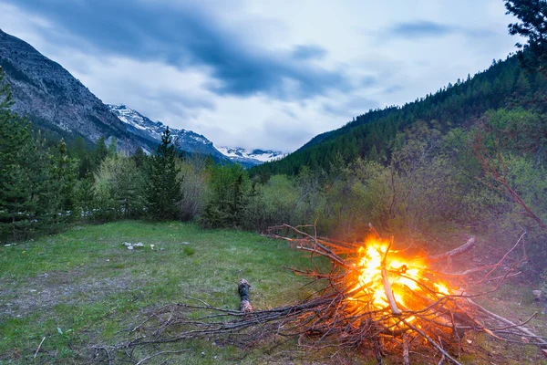 Brennendes Lagerfeuer in abgelegene Lärchen- und Kiefernwälder mit Höhenlandschaft und dramatischem Himmel in der Abenddämmerung. Sommerabenteuer in den italienischen Alpen. — Stockfoto