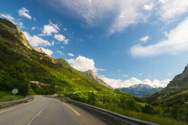 İki şeritli yol geçiş dağ ve orman manzaralı Alpin Peyzaj ve huysuz gökyüzü döşeli. Araba takılı kamera panoramik görüntüsü. Yaz macera ve ROADTRIP İtalyan Fransız Alpleri'nde.
