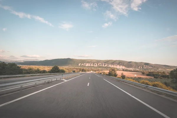 Strada asfaltata a due corsie che attraversa montagne e boschi. Vista panoramica dalla macchina fotografica montata sull'auto. Avventura estiva e gita nelle Alpi francesi. Immagine tonica, stile vintage . — Foto Stock