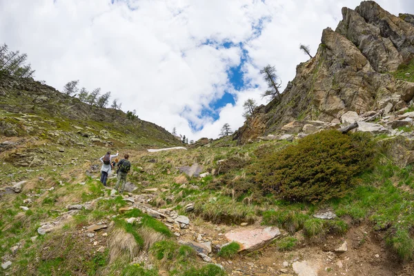 Caminhantes subindo colina acima em trilha de montanha rochosa íngreme. Aventuras de verão e exploração nos Alpes. Céu dramático com nuvens de tempestade . — Fotografia de Stock