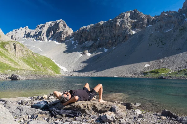 Tramp relaxační ve vysoké nadmořské výšce modré jezero v idylické neznečištěné prostředí, které kdysi pokrývaly ledovce. Letní dobrodružství a průzkum na italské francouzských Alp. Jasně modré obloze. — Stock fotografie