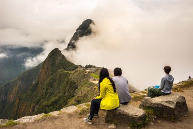 Machu Picchu, Peru - 7 Eylül 2015: Machu Picchu terasından tefekkür gündüz üzerinde oturan üç insanlar. En çok ziyaret edilen seyahat hedef Peru İnka'nın şehridir.