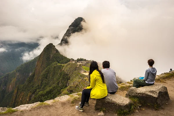 Machu Picchu, Perú - 7 de septiembre de 2015: Tres personas sentadas en la contemplación de Machu Picchu desde la terraza de arriba durante el día. La ciudad del Inca es el destino turístico más visitado en Perú . — Foto de Stock
