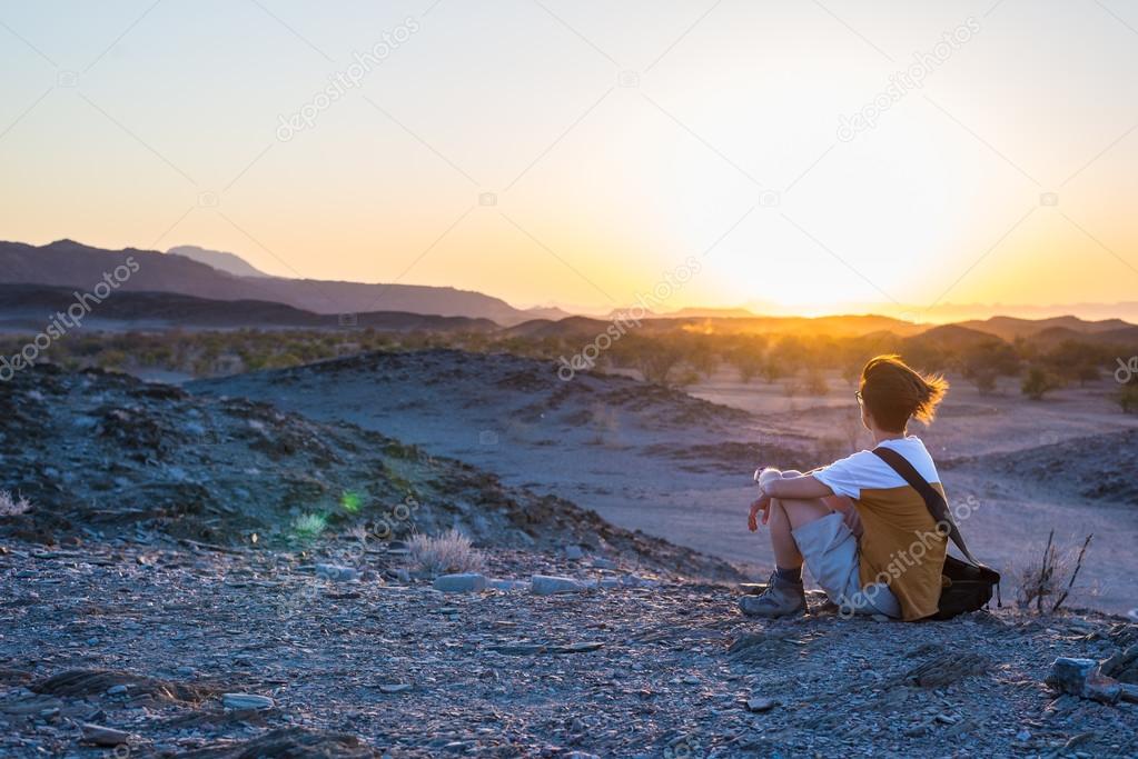 Tourist watching the stunning view of barren valley and mountains in the Namib desert, among the most important travel destination in Namibia, Africa. Backlight view at sunset.