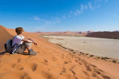 Relaxed tourist sitting on sand dunes and looking at the stunnin clipart