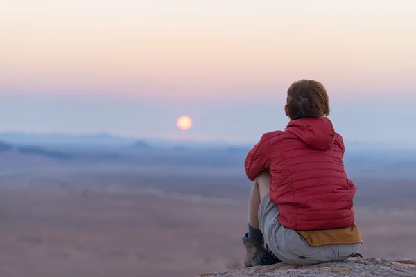 放松的游客坐在岩石上，看着在纳米布沙漠的日落，纳米比亚，非洲最好的旅游目的地。冒险和旅行的人的概念。后视图，选择性对焦. — 图库照片