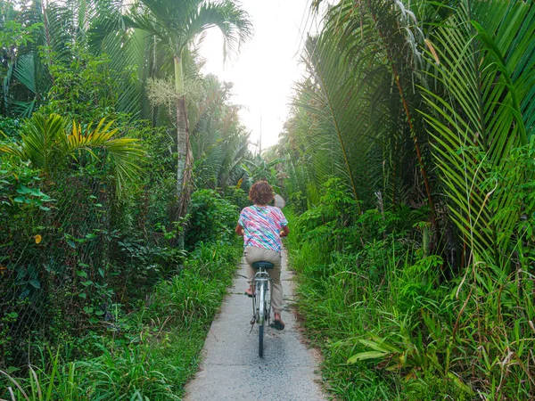 メコンデルタ地域 南ベトナムで自転車に乗る一人 緑豊かな緑のヤシの木の森と熱帯果実果樹園の間の小さなトレイルでの女性のサイクリング — ストック写真