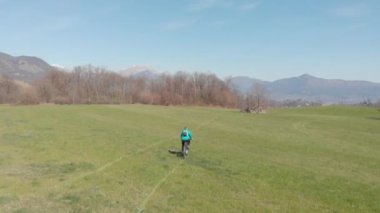 Hava: Güneşli bir günde çimenlerin üzerinde bisiklet sürerek eğlenen bir adam, manzaralı dağlık arazi, doğada fitness refah sporu, doğal düz renk profili