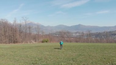 Hava: Güneşli bir günde çimenlerin üzerinde bisiklet sürerek eğlenen bir adam, manzaralı dağlık arazi, doğada fitness refah sporu, doğal düz renk profili