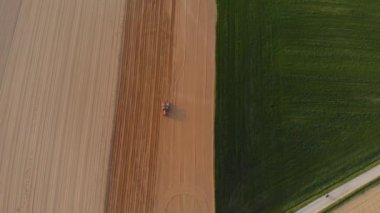 Hava manzarası: ekili tarlalarda çalışan traktör, dağlardaki tarım arazileri, tarım işgali, yemyeşil tahıl, kahverengi toprak geometrik desen, gün batımı ışığı