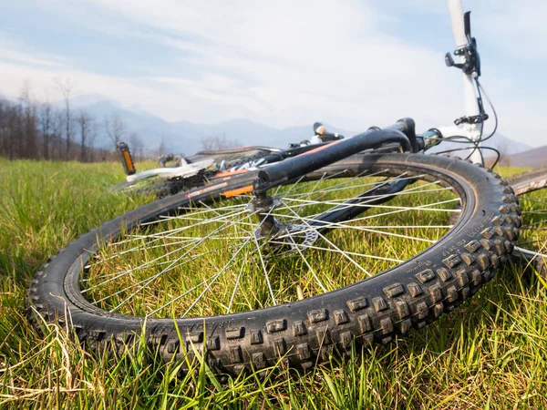 Mountain bike wheel close up. Mtb lying on the grass of alpine meadow. Wide angle view.
