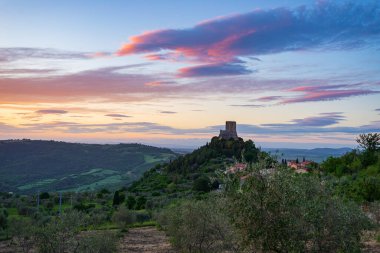 Rocca d 'Oria, Orcia Vadisi, Toskana, İtalya' da bir ortaçağ köyü ve kalesi. Alacakaranlıkta eşsiz bir manzara, taş kule dramatik gökyüzüne karşı kayalıklarda tünemişti..